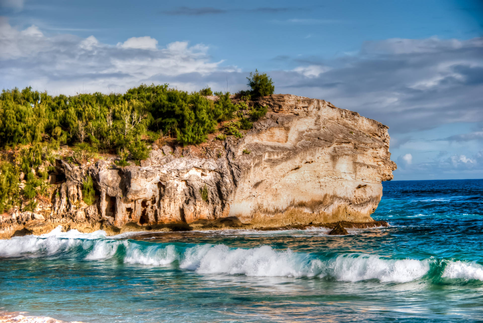 Fondo de pantalla de playa con un enorme acantilado rocoso.