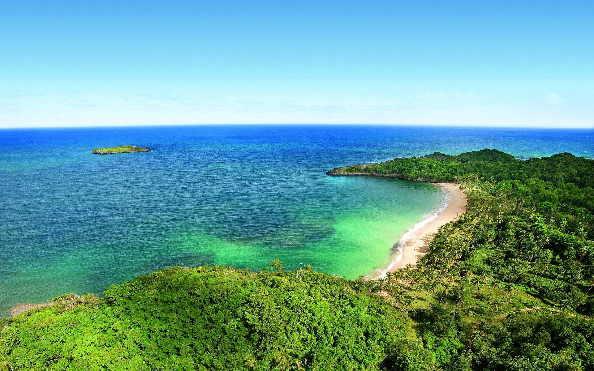 Isla verde y horizonte azul del océano en un clima brillante con cielo despejado.