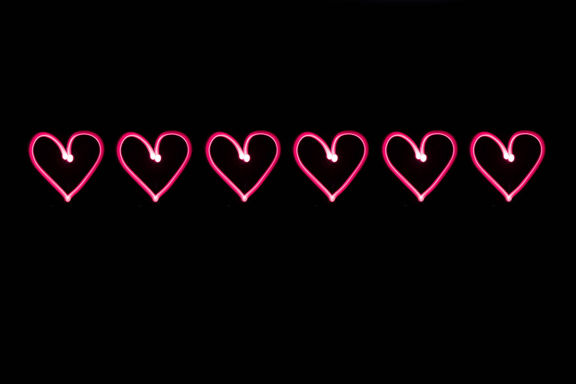Corazones rosas neón dibujados sobre un fondo negro para el Día de San Valentín. Arte digital para tu amor.