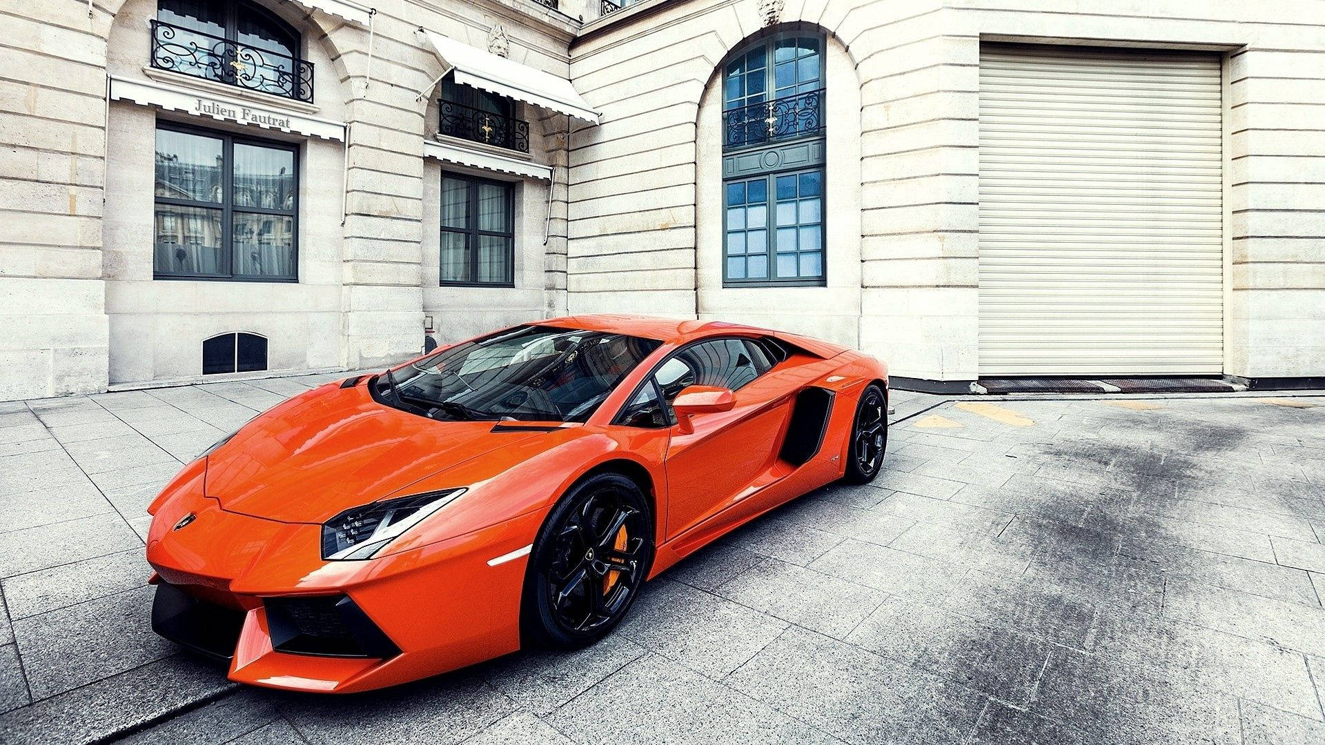 Fondo de pantalla del Lamborghini Aventador naranja con edificios.