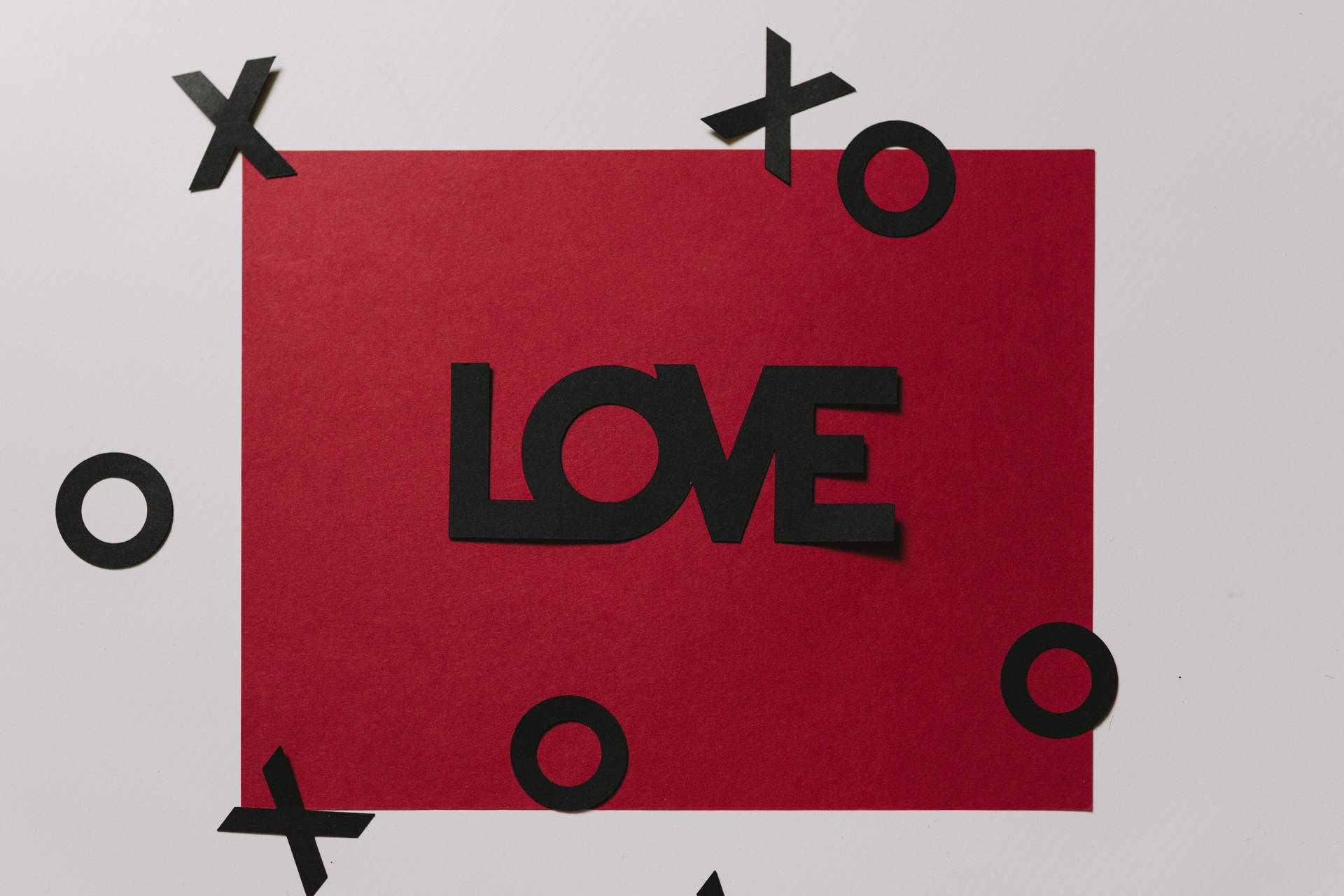 Carta de amor roja con la inscripción 'Amor' en negro y recortes flotantes de XOXO sobre superficie blanca.