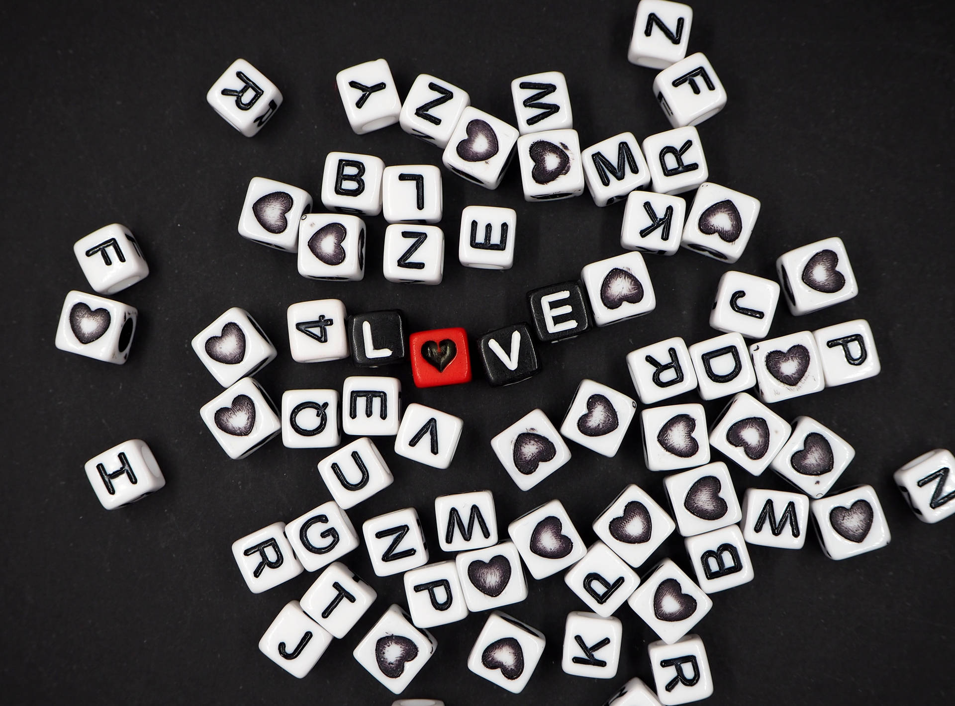 Dados negros formando la palabra "amor" con un corazón reemplazando la "O" y letras de dados blancos esparcidos sobre una superficie negra para el Día del Corazón.