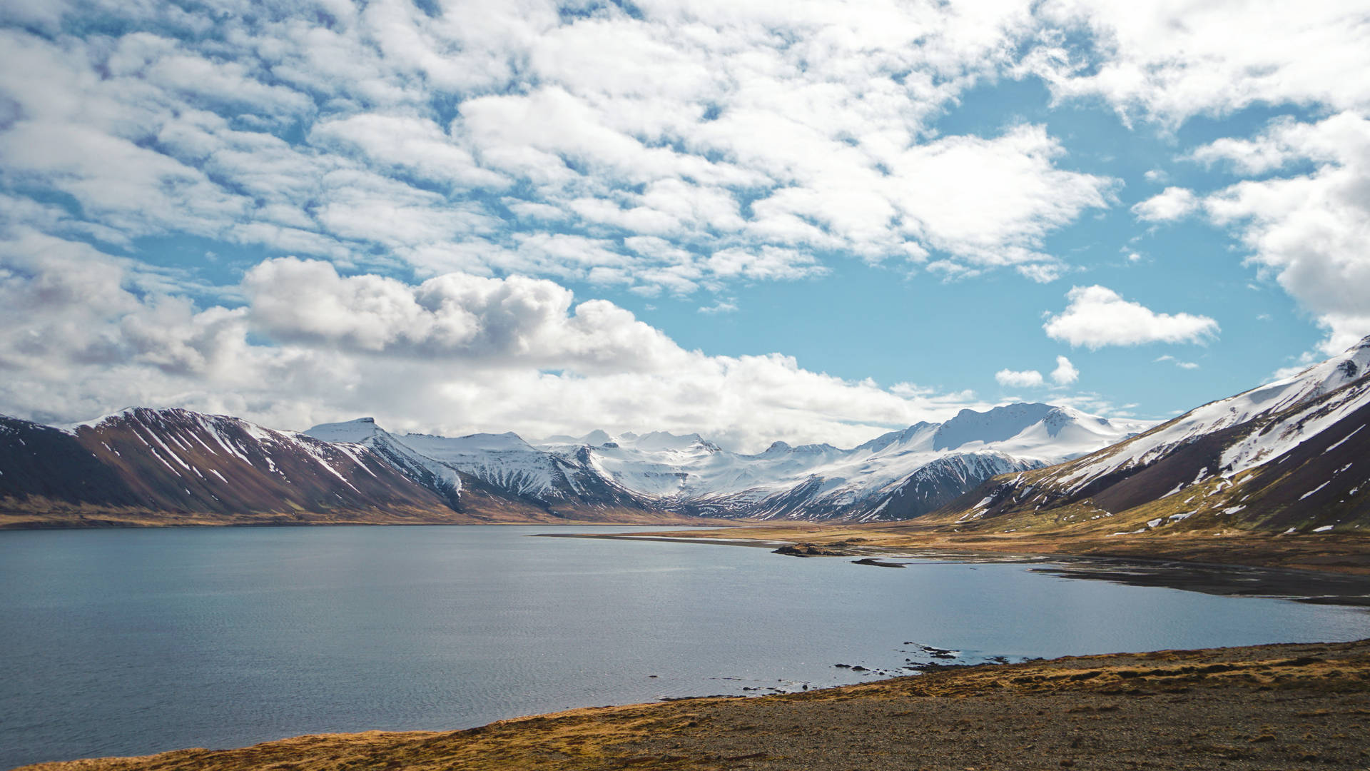 Lago de montaña con montañas nevadas a lo lejos y un cielo nublado.