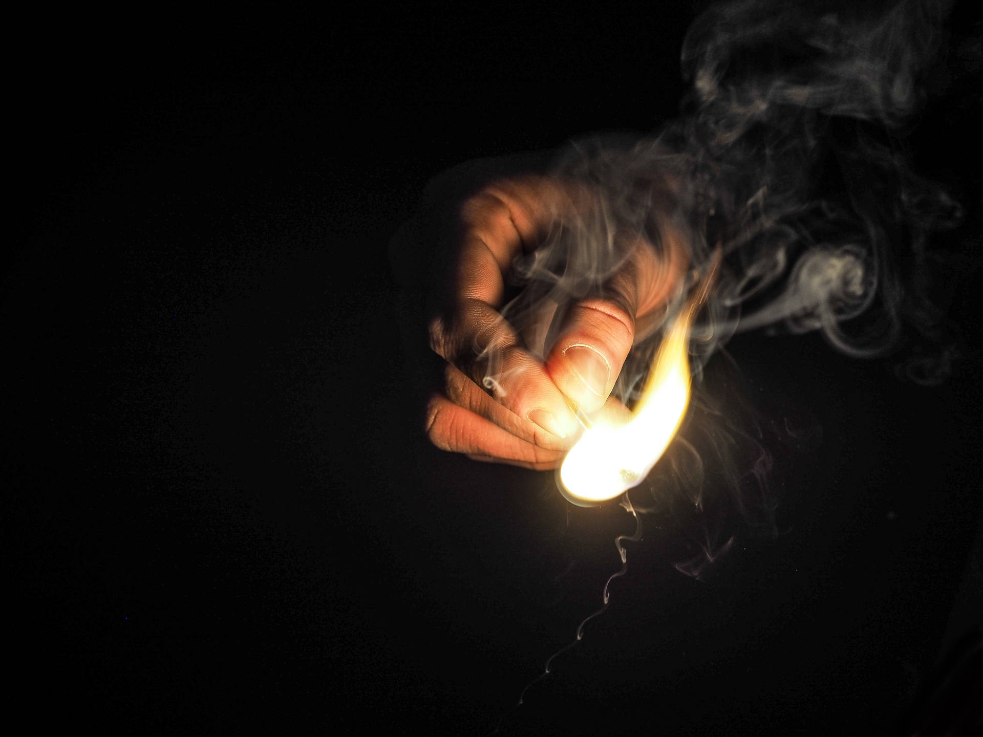 Mano encendiendo un fósforo con fuego amarillo claro dentro de un lugar oscuro.