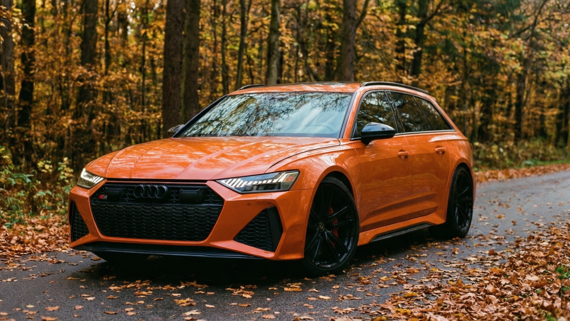 Un Audi RS6 Avant naranja en un camino boscoso otoñal con hojas cayendo.