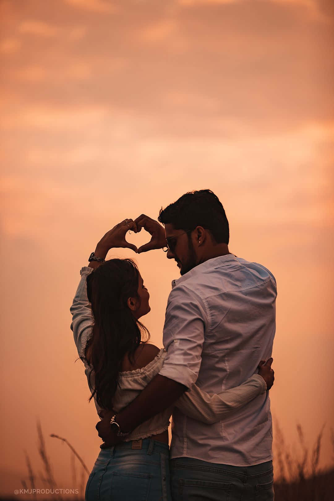 Pareja al atardecer formando un corazón en el campo de hierba Fondos de pantalla