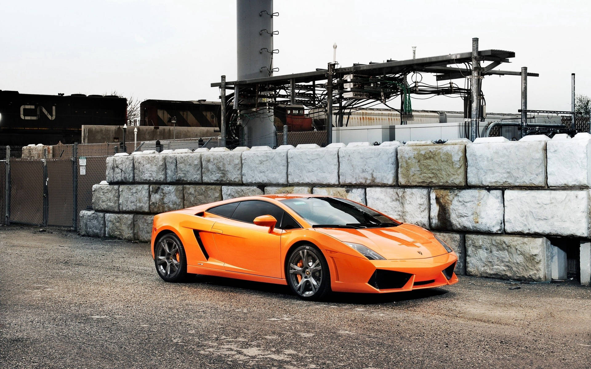 Fondo de pantalla de Lamborghini Gallardo naranja en zona industrial.