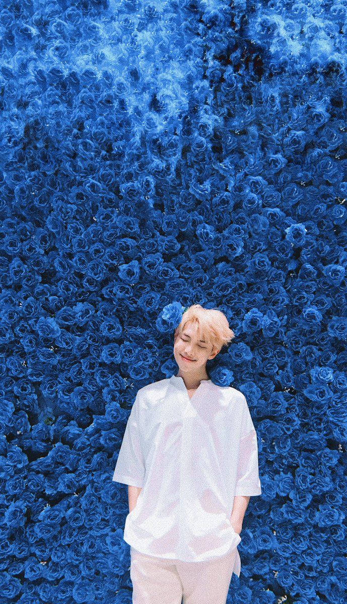 Miembro de BTS de pie frente a una pared llena de flores azules.