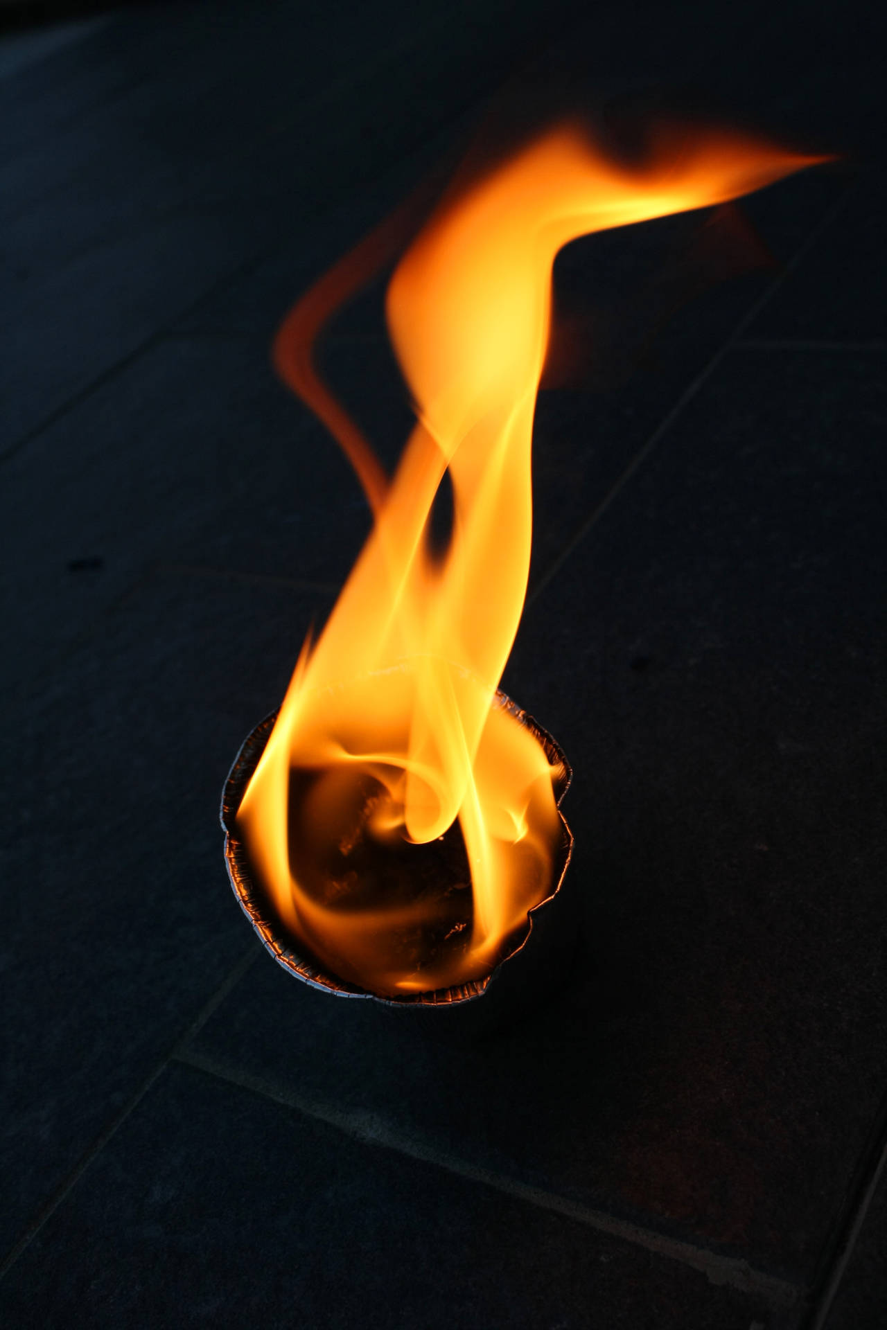 Trozo redondo de papel ardiendo en el suelo. Toma de cerca de la llama del fuego. Cosa ardiendo dentro de una habitación oscura.
