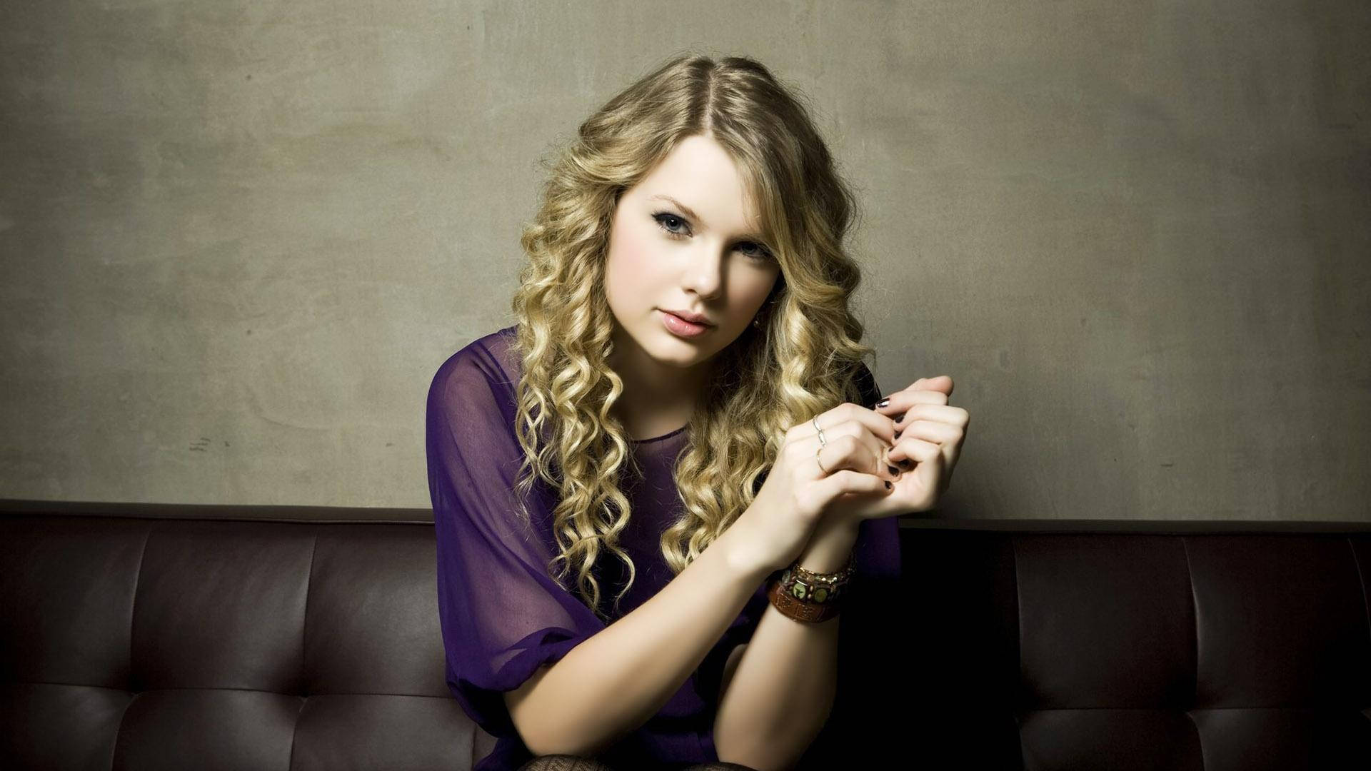 Fondo de pantalla de Taylor Swift sentada con cabello rizado y top de malla morado.