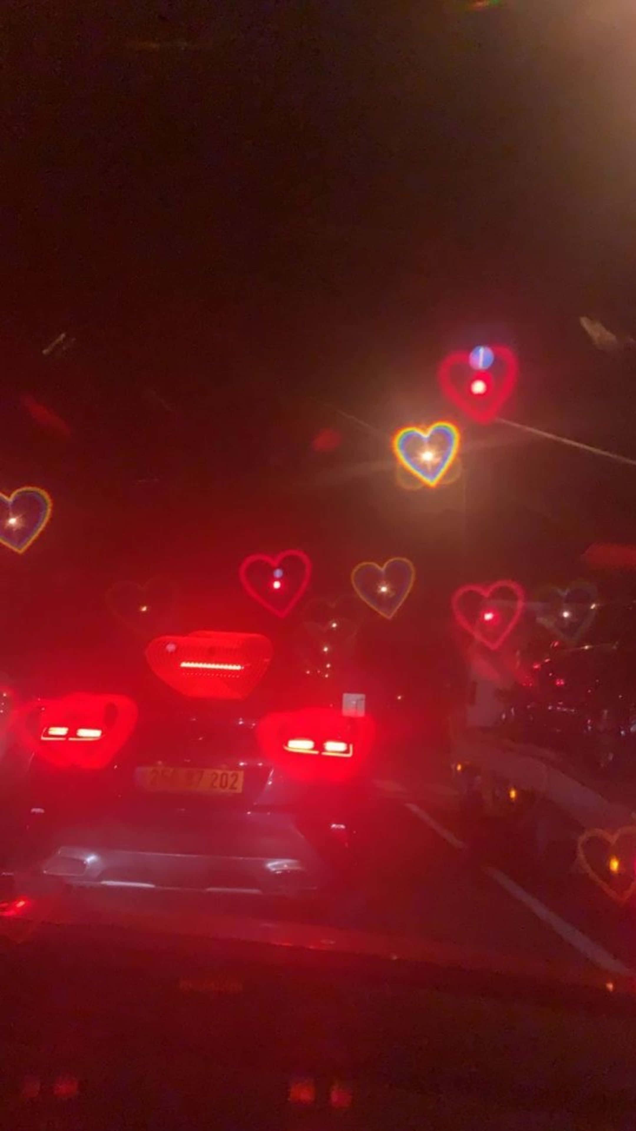 Un auto conduciendo por la carretera de noche con corazones en el parabrisas Fondos de pantalla