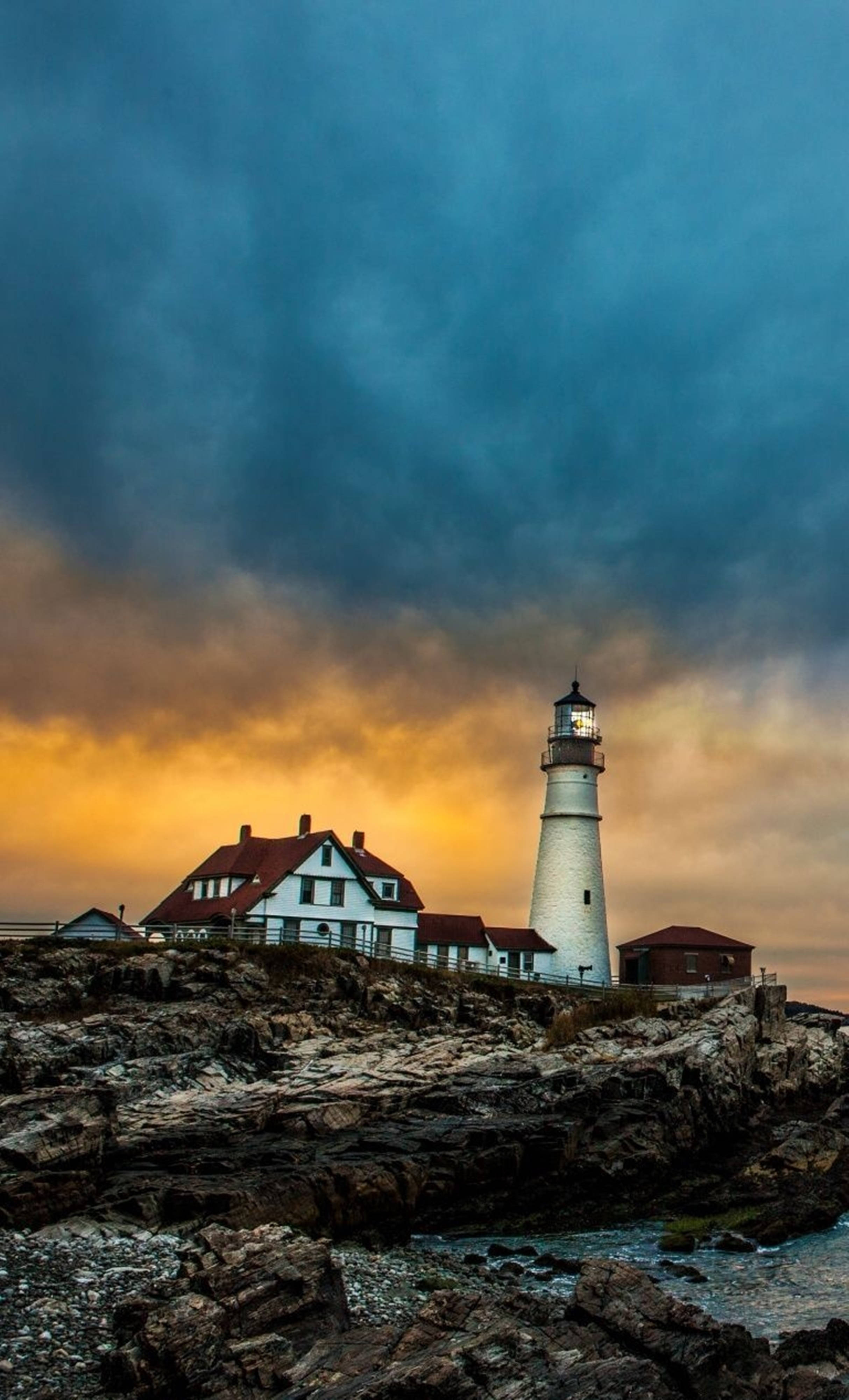 un faro sobre una costa rocosa con un cielo nublado Fondos de pantalla
