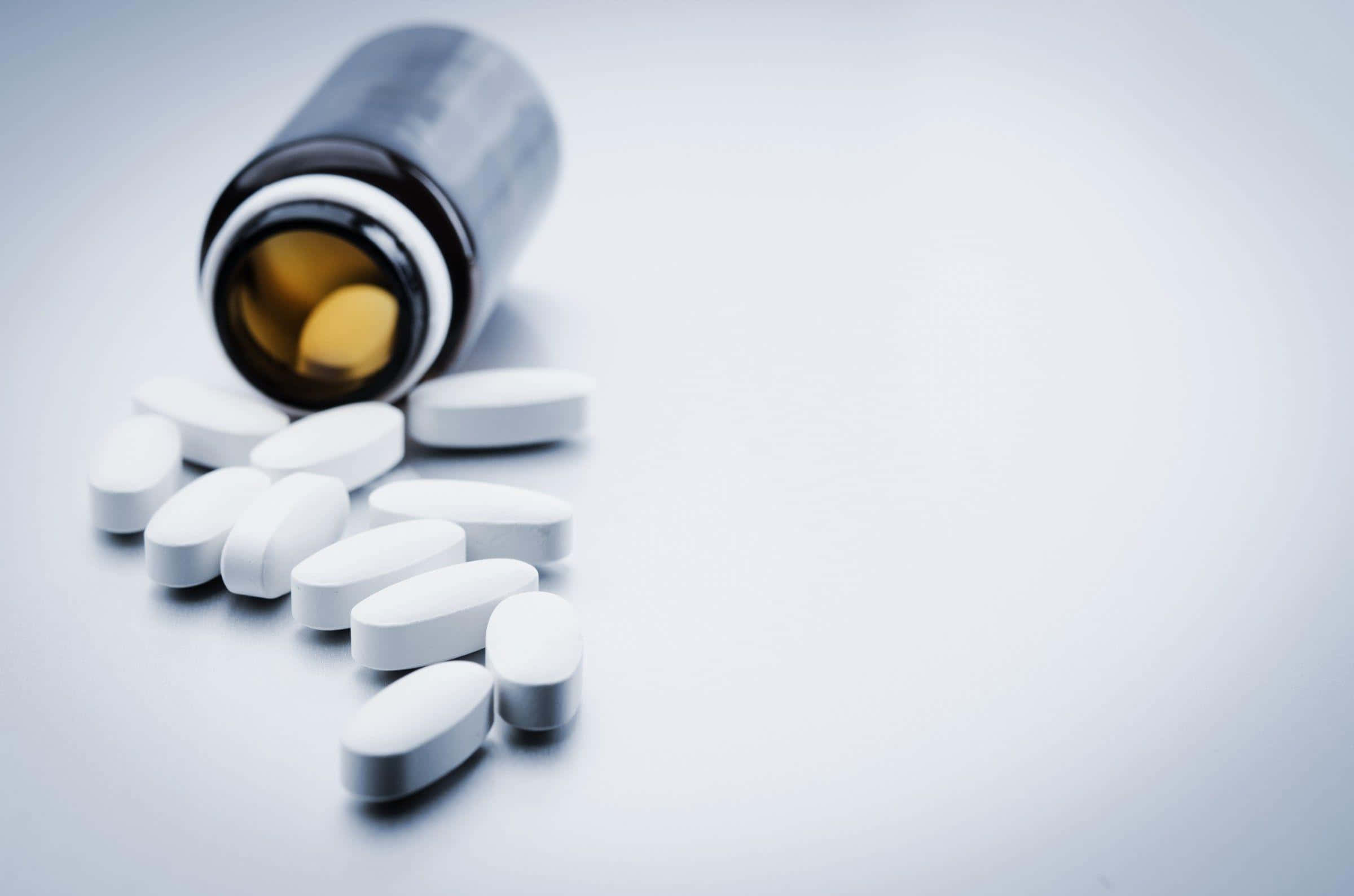 un frasco de pastillas derramándose sobre una superficie blanca Fondos de pantalla