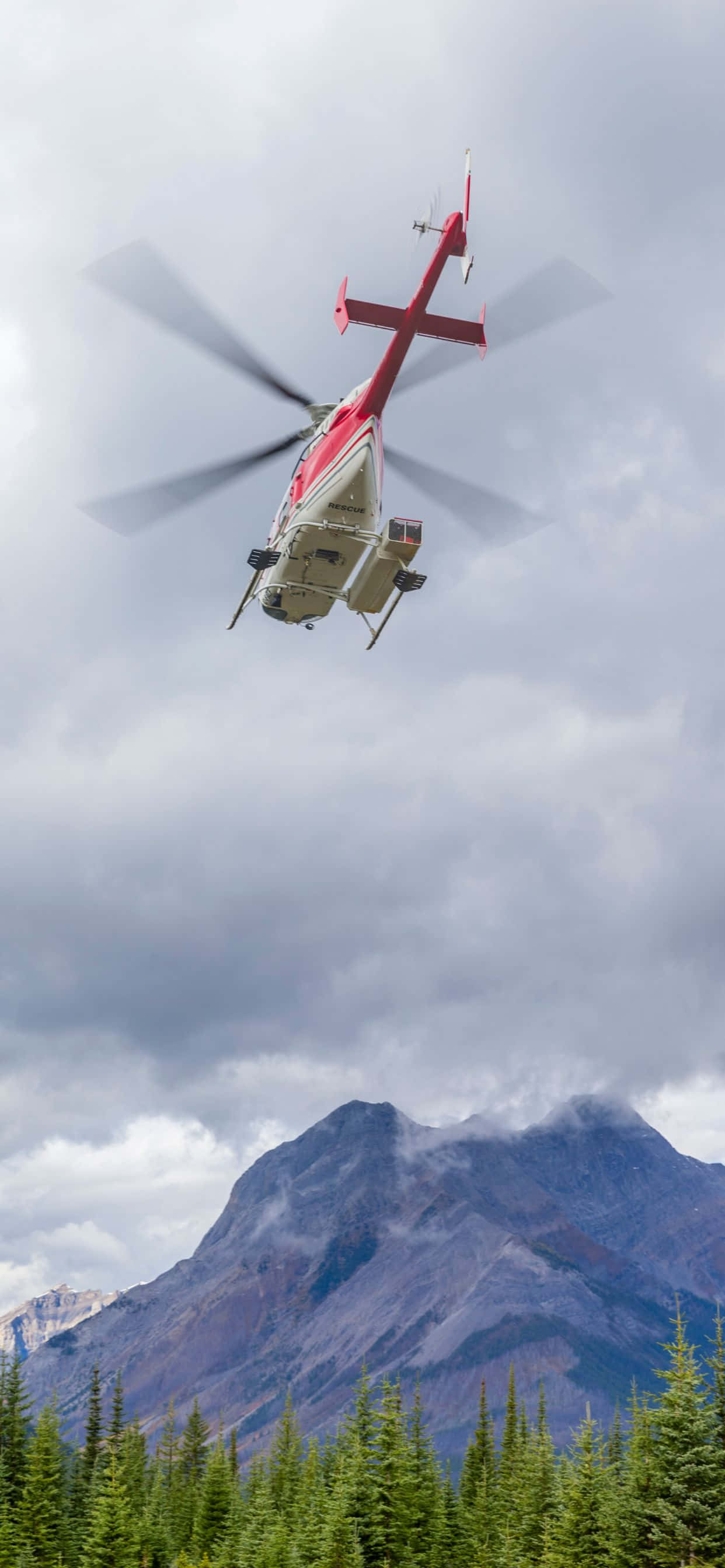 un helicóptero volando sobre un bosque con montañas al fondo Fondos de pantalla