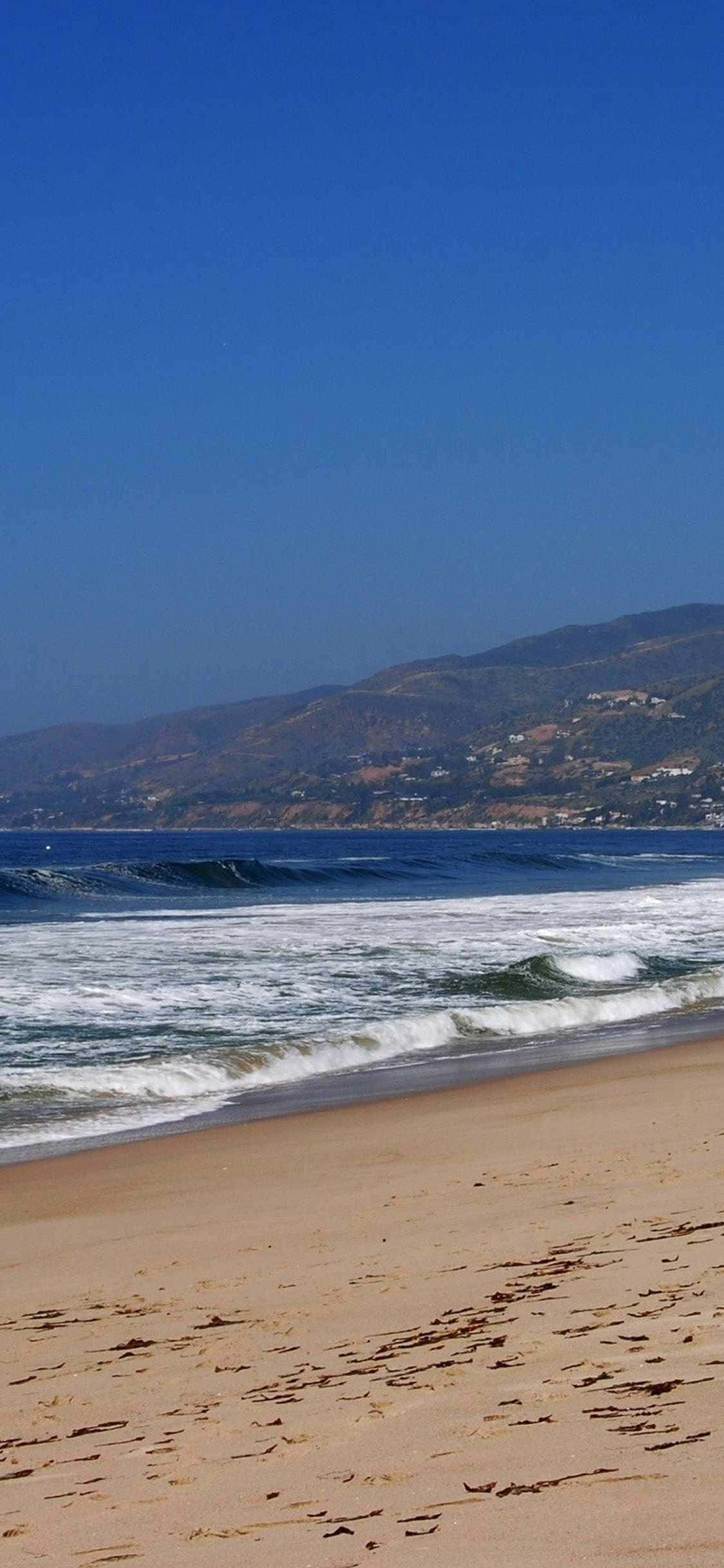 Un hombre camina por una playa con una tabla de surf Fondos de pantalla