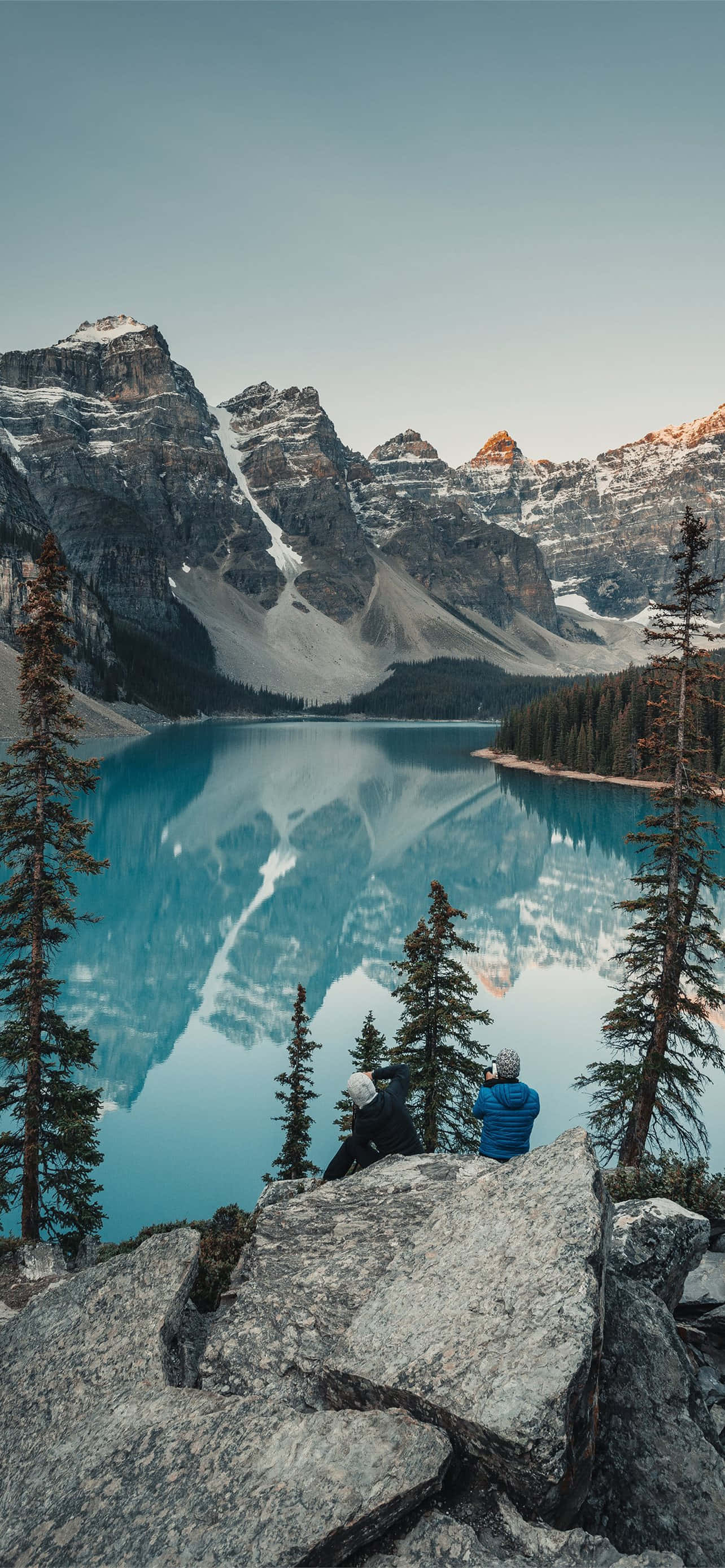 un hombre sentado en una roca con vista a un lago Fondos de pantalla