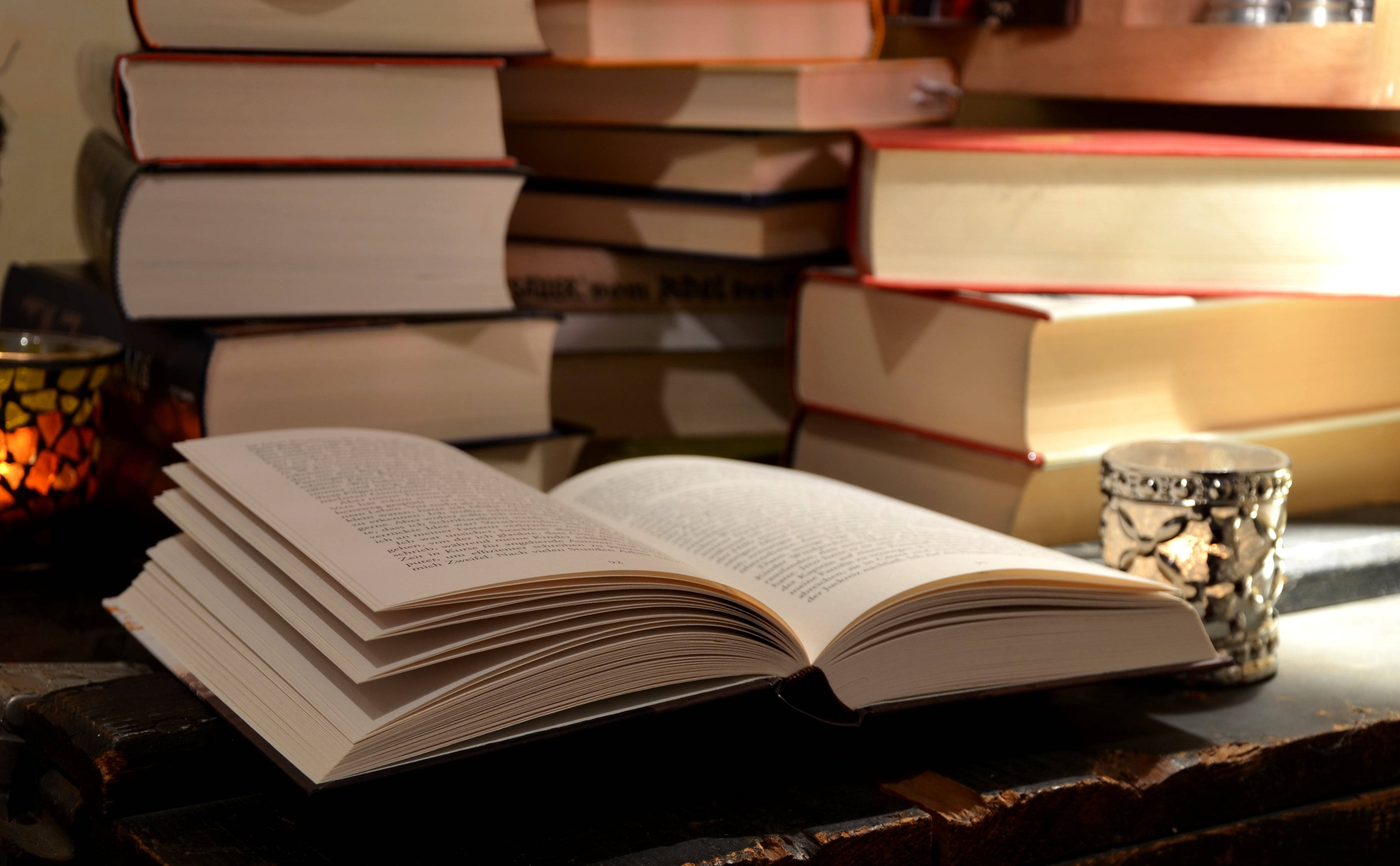 Un libro abierto sobre un escritorio, rodeado de otros libros de consulta Fondos de pantalla