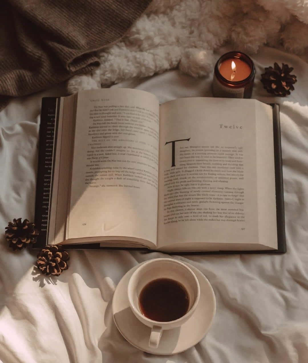 un libro, una vela y una taza de café sobre una cama Fondos de pantalla