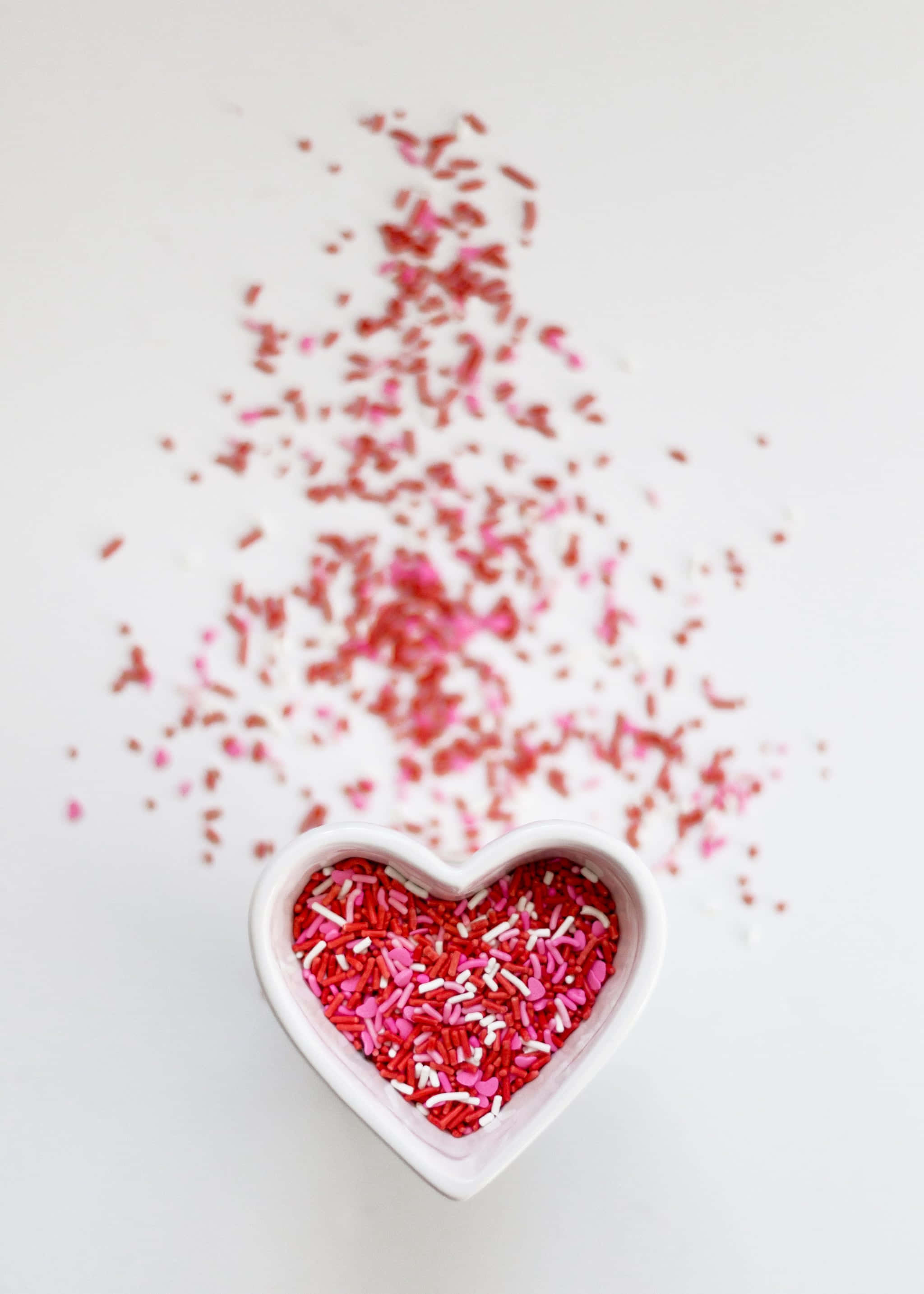 un tazón en forma de corazón lleno de confeti rosa y rojo Fondos de pantalla