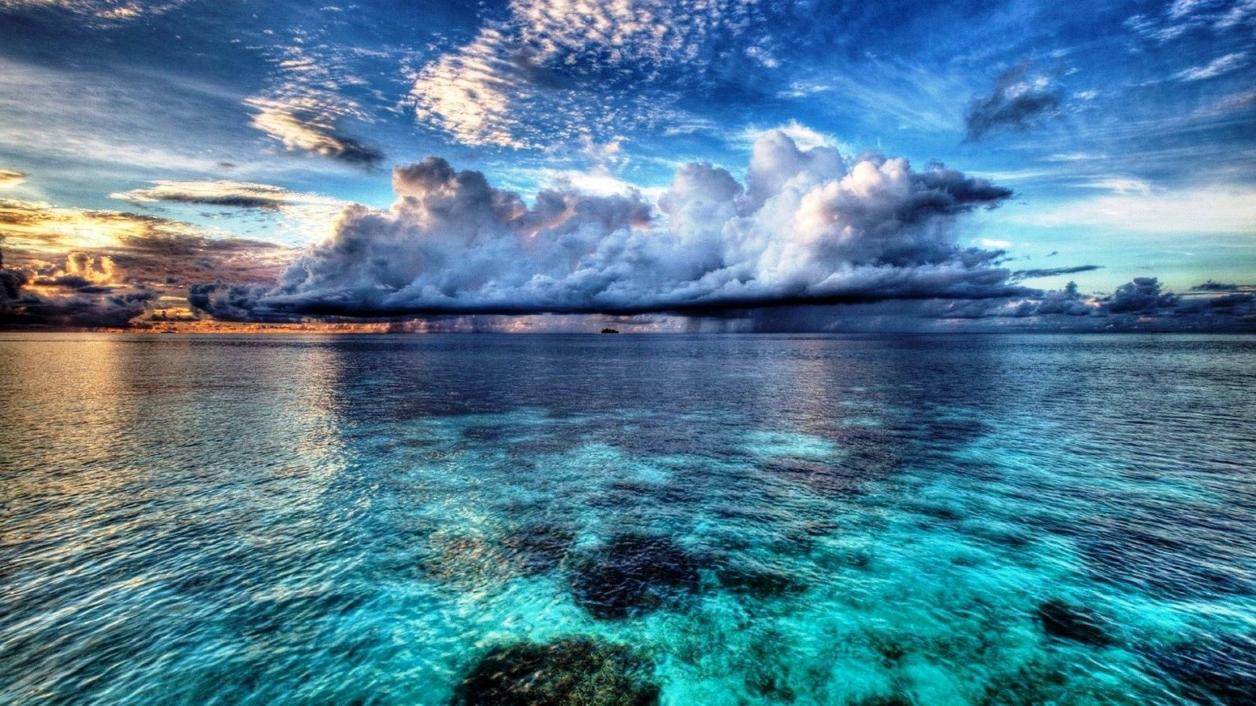 Un vasto y majestuoso océano azul con majestuosas nubes anaranjadas en el cielo. Fondos de pantalla