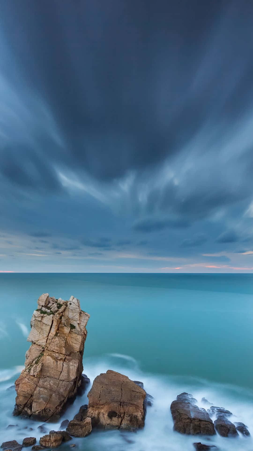 Una formación rocosa con cielo oscuro y océano Fondos de pantalla