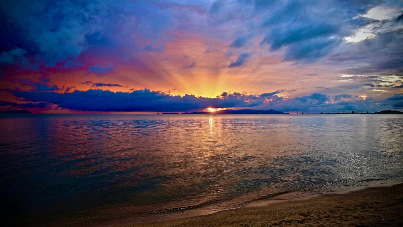 Una impresionante puesta de sol en la playa vista desde lejos Fondos de pantalla