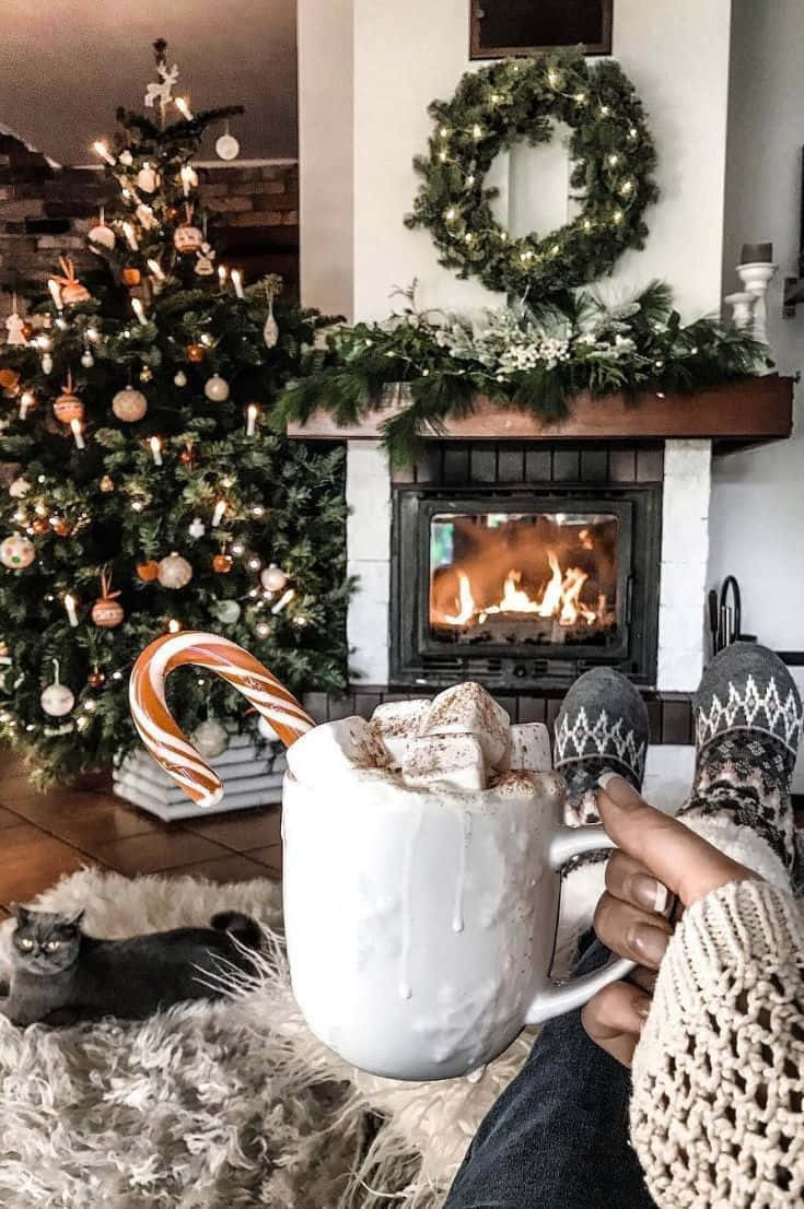 Una persona sentada frente a una chimenea con una taza de chocolate caliente Fondos de pantalla