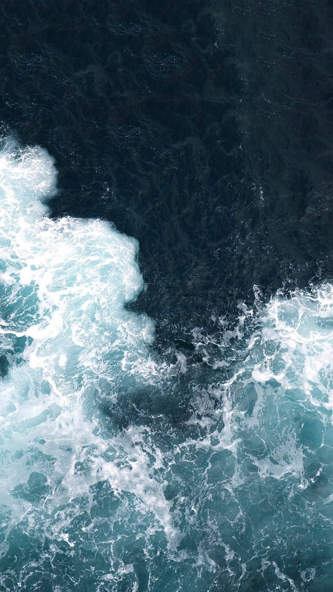 Una vista aérea del poder de las olas del mar rompiendo contra la costa. Fondos de pantalla