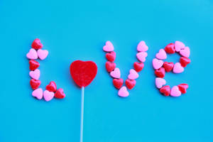Corazones de caramelo rosa y rojo creando la palabra amor sobre una pared azul brillante para el Día de San Valentín.