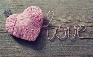 Palabra romántica 'Amor' escrita con cuerda rosa formando un corazón sobre mesa de madera para el Día de San Valentín.