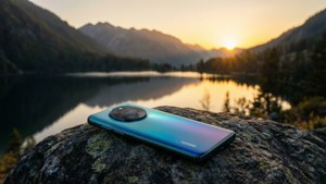 Teléfono Huawei sobre una roca con vista a un lago de montaña al atardecer, paisaje sereno.