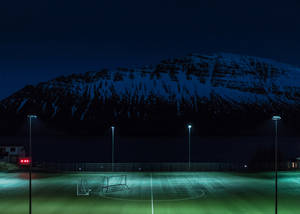 Fondo de escritorio de campo de fútbol nocturno iluminado por postes de luz.