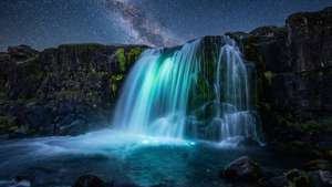 Cascada luminiscente bajo un cielo nocturno estrellado con negros profundos.