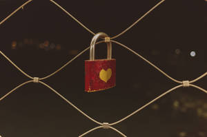 Candado pintado con un corazón rojo y amarillo, asegurado en una cerca de alambre. Candado de amor vintage para parejas.