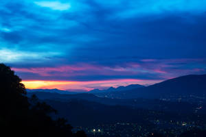 Cielo azul de montaña con luces de la ciudad a lo lejos.