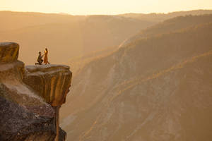Propuesta de amor romántico en la cima de un acantilado rocoso con montañas al fondo durante el atardecer.