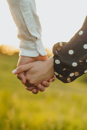 Pareja enamorada caminando en un campo verde con un primer plano de sus manos tomadas para el Día del Corazón.