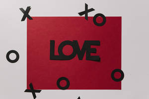 Carta de amor roja con la inscripción 'Amor' en negro y recortes flotantes de XOXO sobre superficie blanca.