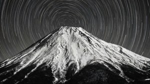 Una foto en blanco y negro de larga exposición de estelas de estrellas rodeando un pico de montaña nevado. — 1600x900 Fondos de pantalla
