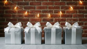 Fila de regalos plateados con moños blancos contra una pared de ladrillo con luces.
