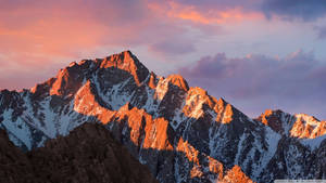 Fondo de pantalla de picos montañosos nevados bajo un cielo naranja al atardecer