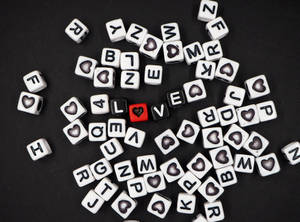 Dados negros formando la palabra "amor" con un corazón reemplazando la "O" y letras de dados blancos esparcidos sobre una superficie negra para el Día del Corazón.
