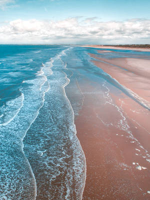Océano azul con espuma marina y pequeñas olas en la orilla.