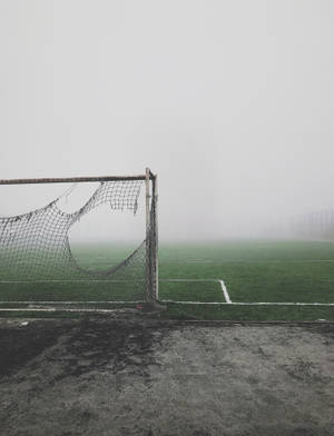 Fondo de pantalla de red de fútbol rota al costado del campo con niebla.
