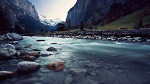 Escena natural de un río fluyendo entre una casa y altos acantilados fondo de pantalla.