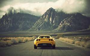 Fondo de pantalla de un auto Lotus amarillo contra un paisaje montañoso.
