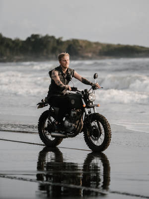 Motociclista tatuado conduciendo por la playa — Vista al océano Fondos de pantalla