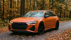 Fondo de pantalla de Un Audi RS6 Avant naranja en un camino boscoso otoñal con hojas cayendo.