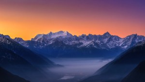 Impresionante vista panorámica de montañas nevadas al amanecer con un valle brumoso.