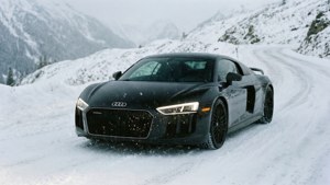 Fondo de pantalla de Un Audi R8 negro circula por una carretera alpina nevada con nieve cayendo.